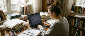 Mlada devojka uči, na stolu su knjige i kompjuter